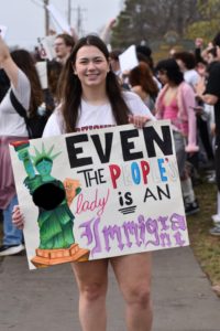 The walkout organizer, Kylie Stafford (12), poses with her protest sign at the walkout location. The sign says, "Even the people's lady is an immigrant."